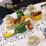 Colorful table display, featuring green teapots, cups and saucers, lemon wedges, tea assortment and finger foods